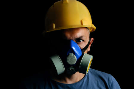 Miner in yellow helmet and respirator on black background.Coal industry, safety and protection