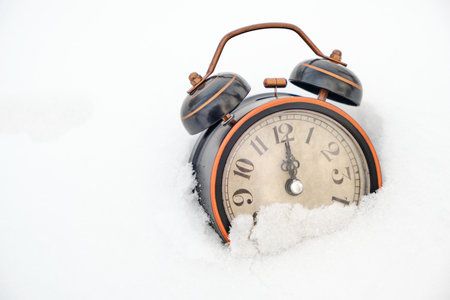 Old retro alarm clock in winter in snow on white background shows twelve hoursの写真素材