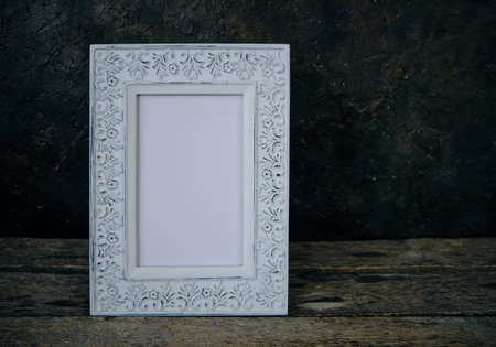 An old, worn, retro photo frame on a wooden table against a concrete wallの写真素材