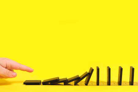 Child's hand pushes a domino with a finger, on a yellow backgroundの写真素材