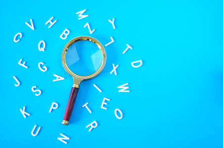 Magnifying glass on a blue background with scattered letters of the alphabetの写真素材