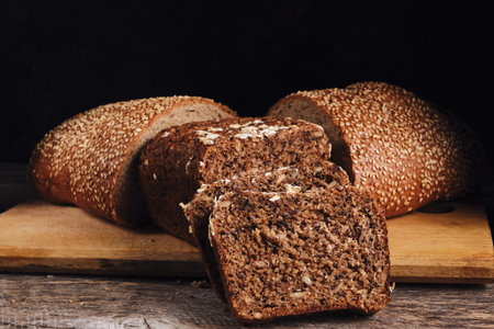 Cut in half a loaf sprinkled with sesame seeds and sliced cereal bread on a cutting board with a...