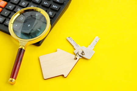 Calculator Magnifier and House Keys Concept of Buying and Selling Housing Mortgages and Renting a House or Apartment Yellow Backgroundの写真素材