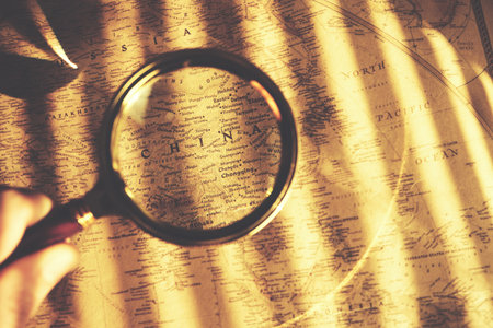 Territory of China on old map is viewed through magnifying glass in bright sunlight through blinds.の写真素材