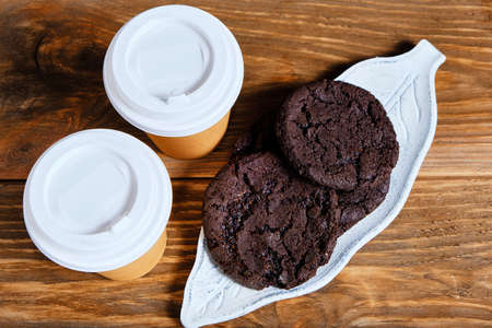 Two glasses takeaway coffee and an American cookie on dark background