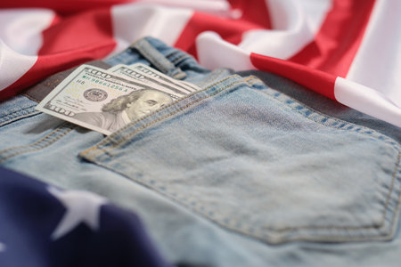 Old worn jeans are lying on flag United States America and there are hundred dollar bills in pocketの写真素材