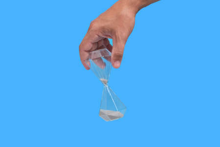 Hourglass in hand, blue background, concept of loss and old age passing time