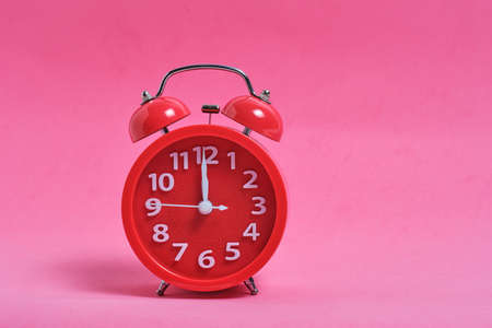 Red alarm clock on a pink background shows twelve clock evening or lunch timeの写真素材