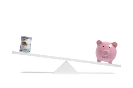 Piggy bank on scales outweighs roll of hundred dollar bills, on white background, business and savingsの写真素材