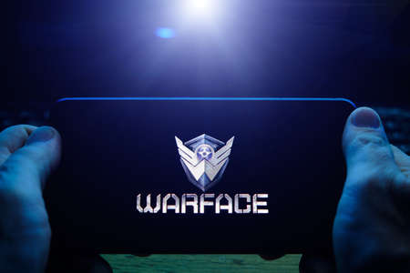 Kostanay, Kazakhstan, November 02, 2021. In hand is mobile phone with screensaver logo popular Warface gameのeditorial素材