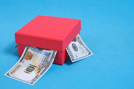 Dollars banknotes are stuck out of a red gift box on a blue backgroundの写真素材
