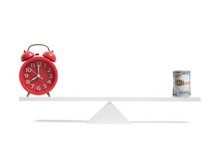Red alarm clock and roll hundred dollar bills are balanced scale white backgroundの写真素材