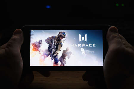 Kostanay, Kazakhstan, November 02, 2021. In hand is mobile phone with screensaver logo popular Warface gameのeditorial素材