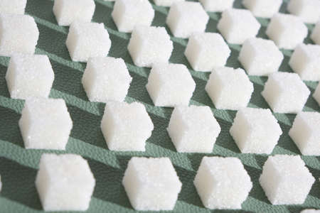 Refined sugar on green background. Cubes of sweet and white sugar in geometricshape. Hard shadowsの写真素材