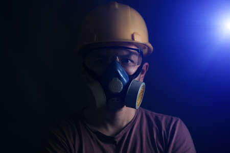 Portrait miner in protective helmet, glasses and respirator, with bright spotlightの写真素材