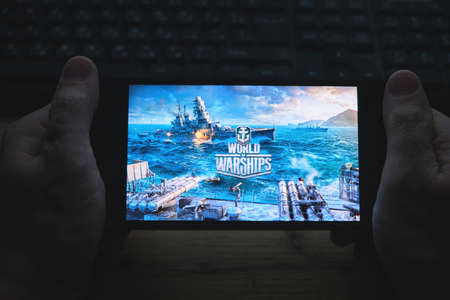 Kostanay, Kazakhstan, November 02, 2021. In hand is mobile phone with screensaver logo popular World of Warships gameのeditorial素材