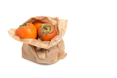 Persimmon fruit in a grocery paper bag on a white backgroundの写真素材