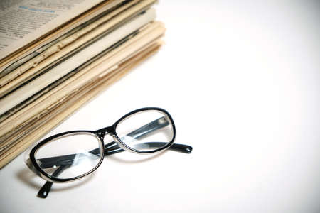 Stack of old newspapers and reading glasses on a white background
