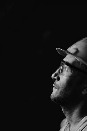Profile portrait of a miner in a helmet and goggles, looking at the light.A dirty worker in a shirt.の写真素材