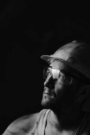 Profile portrait of a miner in a helmet and goggles, looking at the light.A dirty worker in a shirt.の写真素材