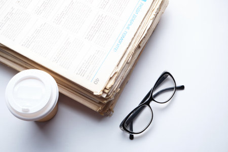 Stack old newspapers, glass of coffee and glasses for reading newspaper news