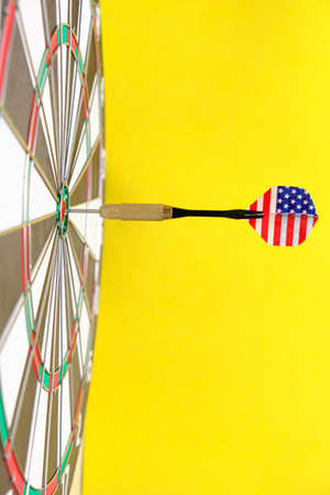 Concept achieving goal.Achieving goals in business, politics and life. Dartboard with darts painted with American flag stuck right into target.On yellow backgroundの写真素材