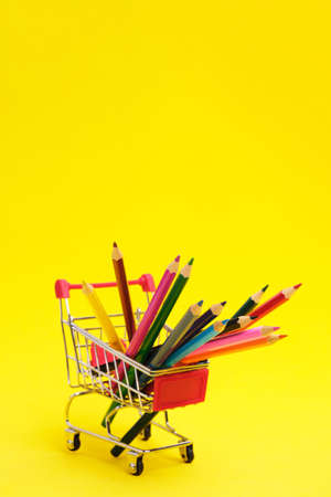 Colored pencils in shopping cart on yellow background.School supplies for drawingの写真素材