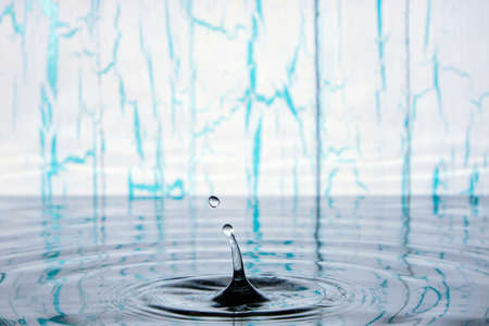 Splash and ripples on water from falling raindrop on light wooden background with peeling paintの写真素材