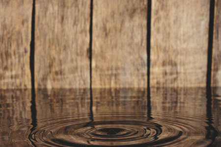 Splash and ripples on water from fallen raindrop on wooden backgroundの写真素材