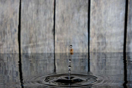 Splash and ripples on water from fallen raindrop on wooden background