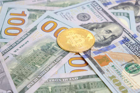Unfolded bundle of hundred dollar bills and one bitcoin coin