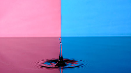 Splash of water from fallen raindrop on blue pink backgroundの写真素材