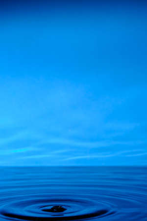 Water splashes after raindrop falls.Blue abstract background with splash of drop of waterの写真素材