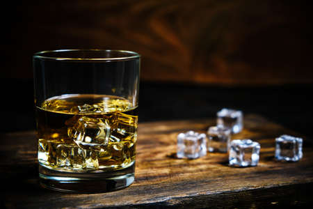 Glass chilled whiskey with ice cubes on wooden background in cellarの写真素材