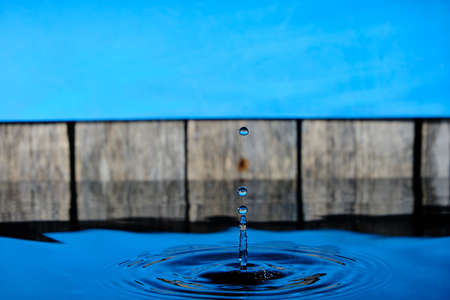 Circles and splash on water from raindrops on background an old fence and blue skyの写真素材