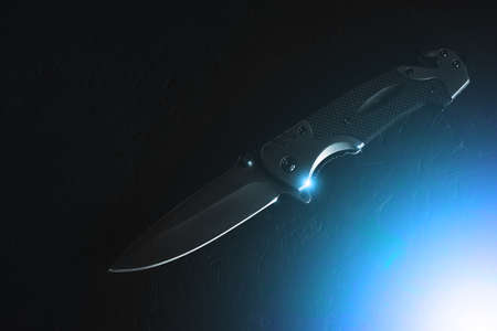 Tactical folding knife on dark background is illuminated by bright blue lightの写真素材