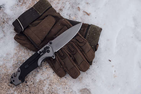 Tactical gloves and a folding knife in the snowの写真素材