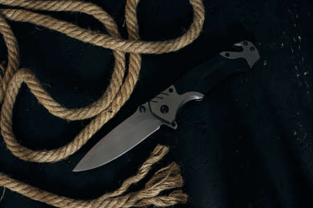 Tactical folding knife for survival, active lifestyle and recreation, on rope background and dark...
