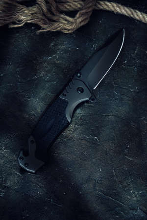 Tactical knife and cut rope on rocky background.Survival and adventure