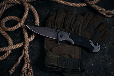 Folding knife, tactical military gloves and rope on dark backgroundの写真素材