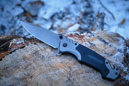 Folding camping knife lies on stump fallen pine tree in winter forest