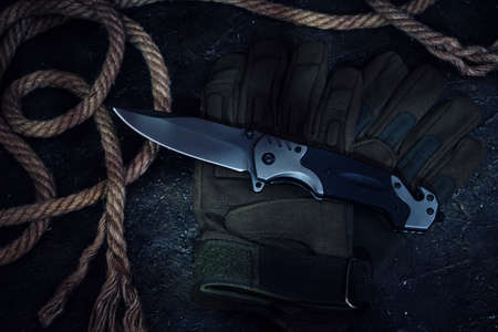 Folding knife, tactical military gloves and rope on dark backgroundの写真素材