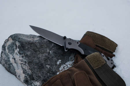 Tactical gloves and a folding knife in the snowの写真素材