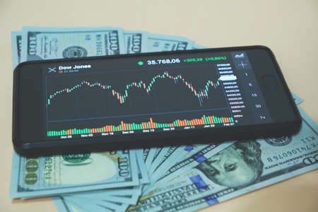 Stock exchange chart on smartphone screen and hundred dollar bills on beige backgroundの写真素材