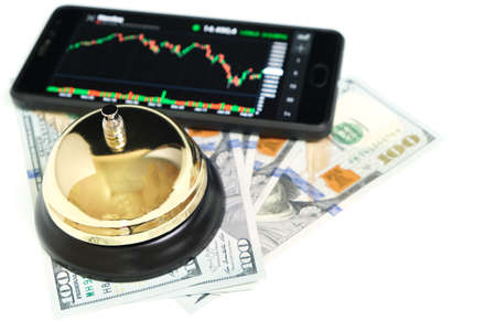 Stock exchange chart on smartphone screen, bell and hundred dollar bills on white background.Concept, stocks, business and financeの写真素材