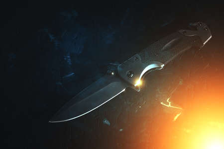 Tactical folding knife is illuminated with bright yellow light on dark backgroundの写真素材