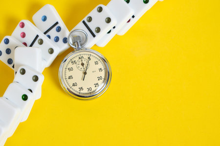 Stopwatch and scattered dominoes on a yellow background. times upの写真素材