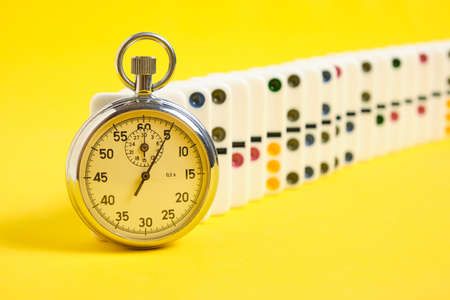 Stopwatch and dominoes on a yellow background. times upの写真素材