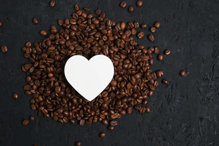 Roasted coffee beans and a white heart on a dark background.Concept of love for coffee drinkの写真素材