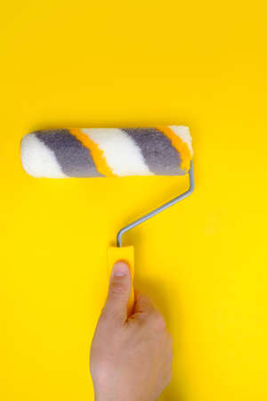 Paint roller in hand for painting walls and repairs on yellow backgroundの写真素材